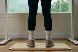 Supportive insoles arranged beside work boots and sneakers on a hardwood floor