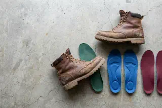 Supportive insoles beside broken-in leather work boots on a hard shop floor