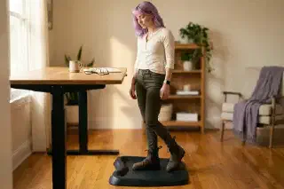 Low-angle view of Mira in Blundstone Chelsea boots on a contoured anti-fatigue mat at her standing desk