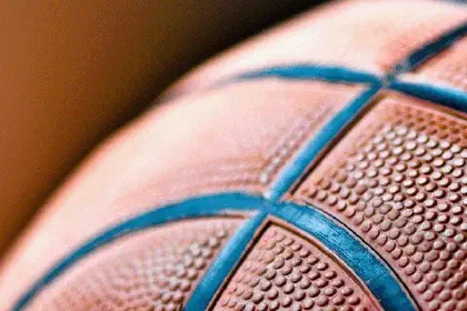 Close-up of an orange basketball with teal seams on a warm background