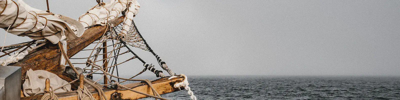 Wooden ship bow with rope rigging sailing across a gray open sea