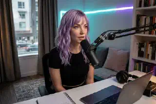 Mira speaking into a dynamic microphone on a boom arm at a compact desk