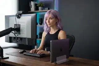 Mira at a docked laptop workstation with an external monitor and monitor-mounted webcam